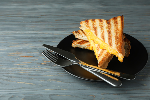 Plate with grilled sandwiches and cutlery on wooden table