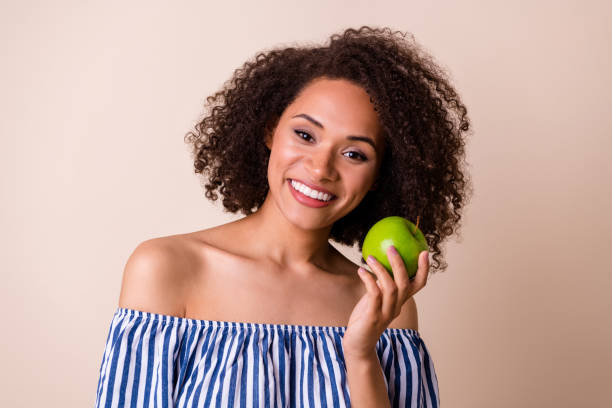 foto di bella signora carina indossare vestito a righe godendo di frutta succosa sorridente isolato colore beige sfondo - apple women green eating foto e immagini stock