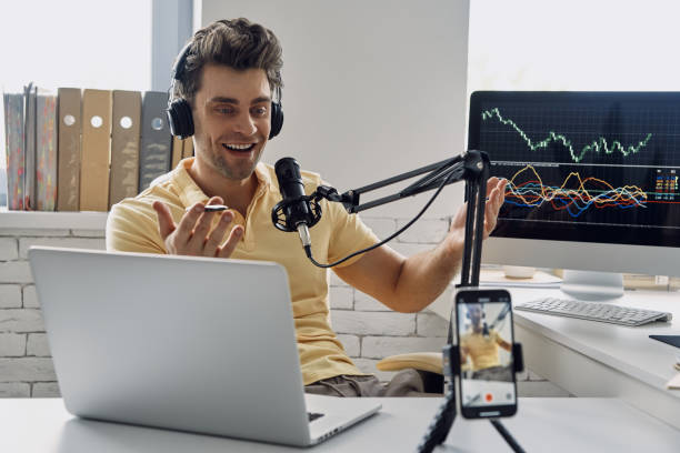 istock Cheerful man in headphones using microphone and gesturing while recording his business podcast 1413800170