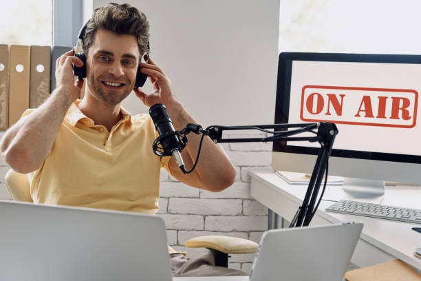 istock Handsome young man in headphones using microphone while recording podcast in studio 1413800514