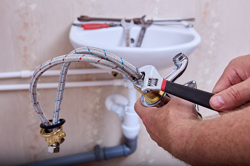 Plumbing work on installing new water faucet in toilet, plumber connects stainless steel braided  hoses to tap  using an adjustable wrench.