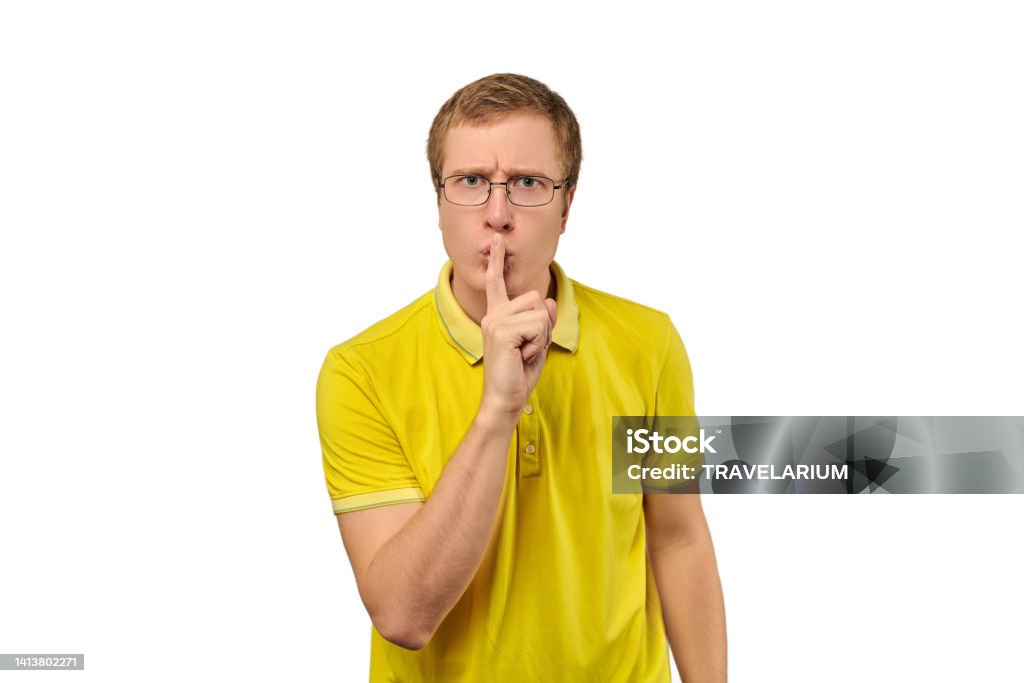 Funny young man in yellow T-shirt asking to be quiet, silence gesture, white background Funny young man in yellow T-shirt asking to be quiet, silence gesture isolated on white background. Young man in glasses saying Shhh, keep quiet, please and making silence gesture, request for silence 25-29 Years Stock Photo