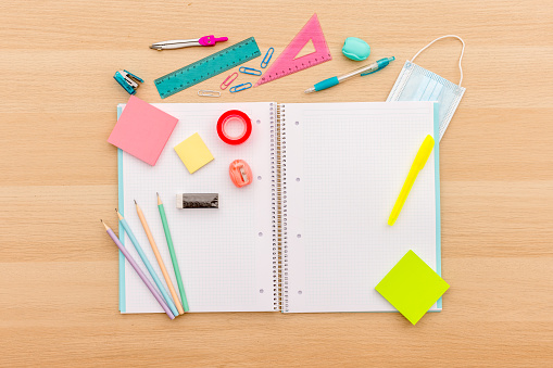 Back to school concept, creative layout with various school supplies, pencils, ruler, tapes, notebook, paper clips, pencil sharpener, notepads, markers and medical protective mask on wooden background with copy space