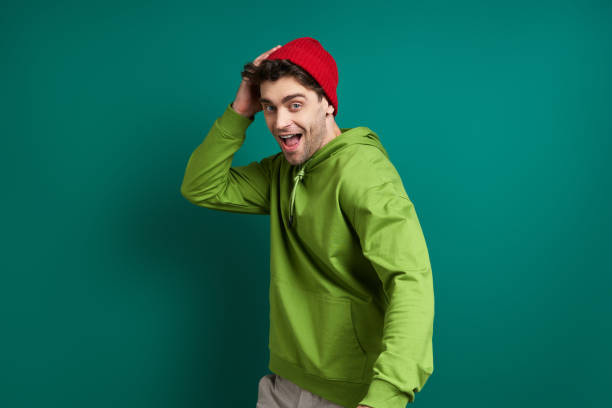 istock Cheerful young man adjusting his hat while standing against green background 1413804162