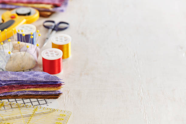 istock Ruler, cutting mat, stack of multi-colored pieces of fabric, pincushion, spools of thread, scissors, rotary cutter, stack of fabric on a white surface. Space for text 1413805630