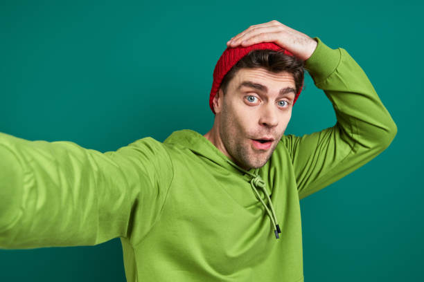 istock Surprised young man making selfie while standing against green background 1413807185
