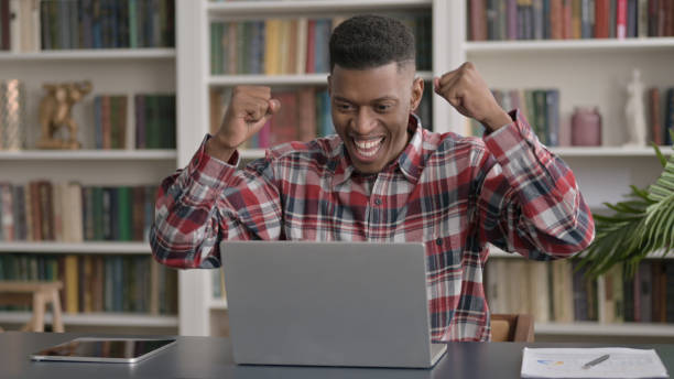 istock African Man Celebrating Success while using Laptop in Office 1413807244