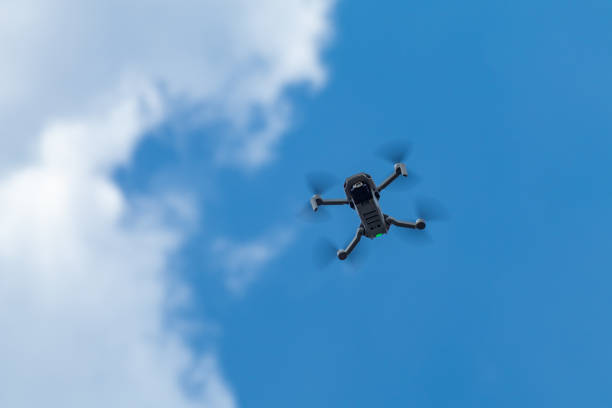 Kharkiv, Ukraine - April 22, 2021: Dji Mavic Mini 2 drone, flying with green led on. New quadrocopter device hovering on blue cloudy sky, blurry background. Bottom view with copy space