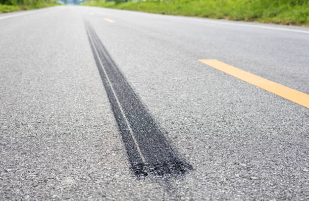 A close-up low-angle view, a long line of black tires stopping violently against the paved road surface. A close-up low-angle view, a long line of black tires stopping violently against the paved road surface with yellow stripes commonly seen in rural Thailand. street skid marks stock pictures, royalty-free photos & images