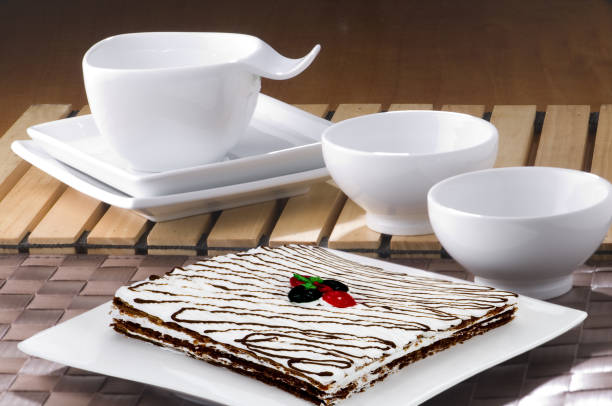 Decorated empty white plates and cups, with cake in the foreground