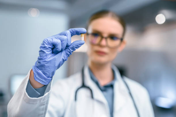 hand des arztes, die eine medizintablette hält und op-handschuhe trägt, um den medizinischen durchbruch zu zeigen. nahaufnahme von medikamenten zwischen den fingern, um neue heilpille oder vitamin für die moderne gesundheitsversorgung zu fördern - surgical glove human hand holding capsule stock-fotos und bilder