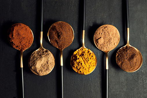 Colorful range of spoons of herbs and spices to add flavor to food while cooking. Top view of seasoning for an Indian curry dish recipe isolated on a black background.