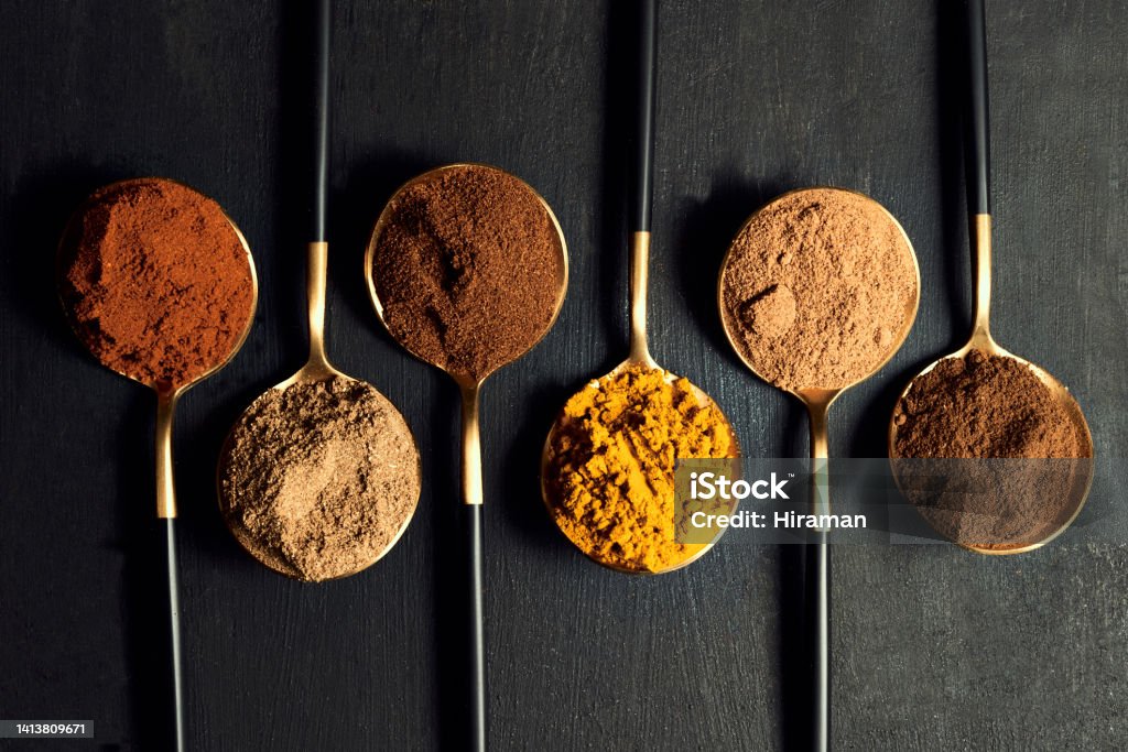 Colorful range of spoons of herbs and spices to add flavor to food while cooking. Top view of seasoning for an Indian curry dish recipe isolated on a black background. Spice Stock Photo