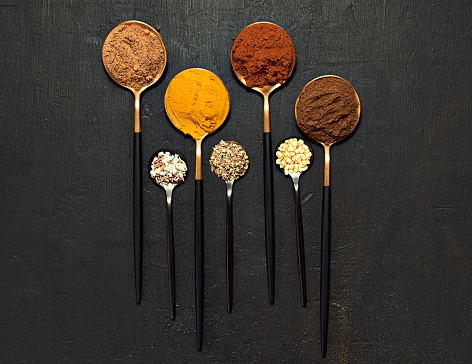 Colorful spices in different size spoons against dark black background with copy space. Closeup of flavor agents used in traditional meals created from scratch. Zoom in on measured powder for food