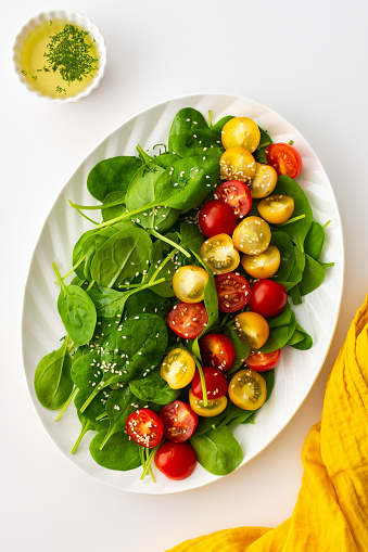 Salad with yellow and red tomatoes and spinach, top view of an oval plate with lettuce on a white background