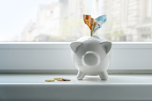 Piggy bank with euro notes and coins on a window sill, concept for thrift during inflation, copy space, selected focus, narrow depth of field