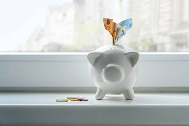Piggy bank with euro notes and coins on a window sill, concept for thrift during inflation, copy space, selected focus stock photo