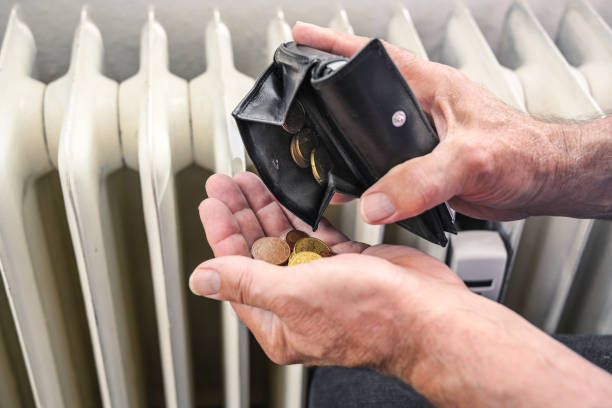 Hands of a man pouring out few coins from a wallet in front of an old heater, suffering from rising energy costs, copy space, selected focus stock photo