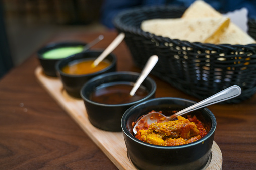 Indian dip, relish, chutney and sauce served in small black bowls with crispy papadam bread on a dark wooden table, copy space, selected focus, very narrow depth of field