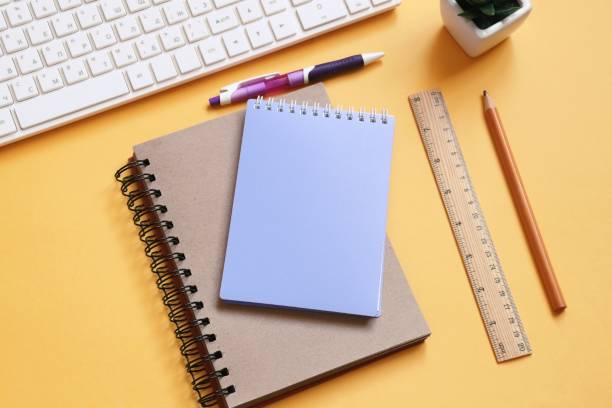 istock White computer keyboard, paper notebook, purple pen, pencil, wooden ruler on a yellow table. Modern office workspace view from above. Online education, distance learning concept 1413815743