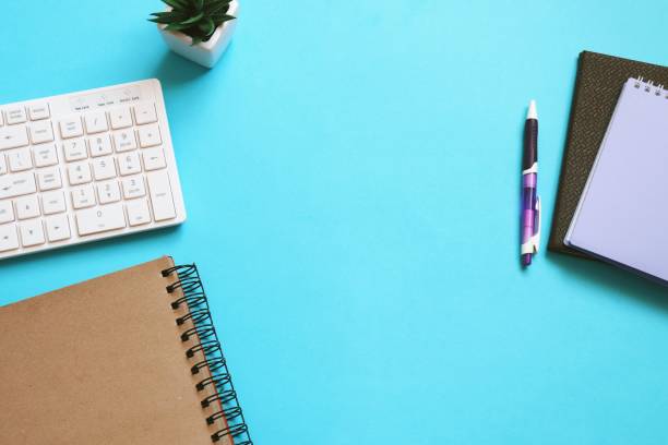 istock White computer keyboard, paper notebook, purple pen, cactus on a blue table view from above photography. Office or college desk. Modern work space, mockup 1413815778
