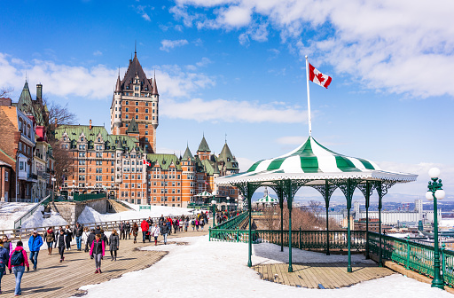 People enjoying sunny weather in early springtime as the snow melts, walking along the promenade with Château Frontenac in the background.