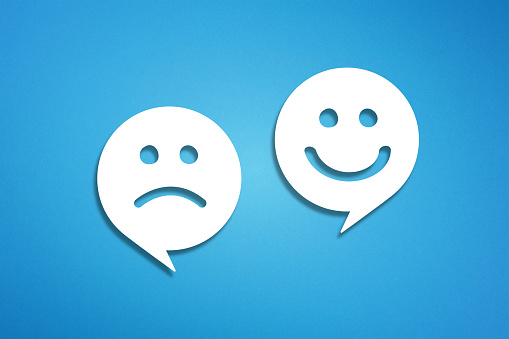 Speech bubbles with happy and sad face emoticon over blue background