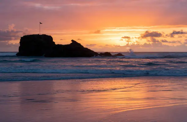 The sun sets on Perranporth Beach in Cornwall, silhouetting the rocky landmark that is Chapel Rock.
