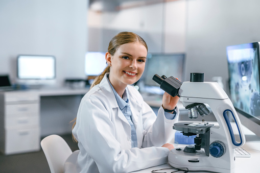 Scientist, medical worker and chemist using microscope to do analysis of test sample in lab. Engineer in biotechnology labrotory smiling doing medical research and testing to create medical cure