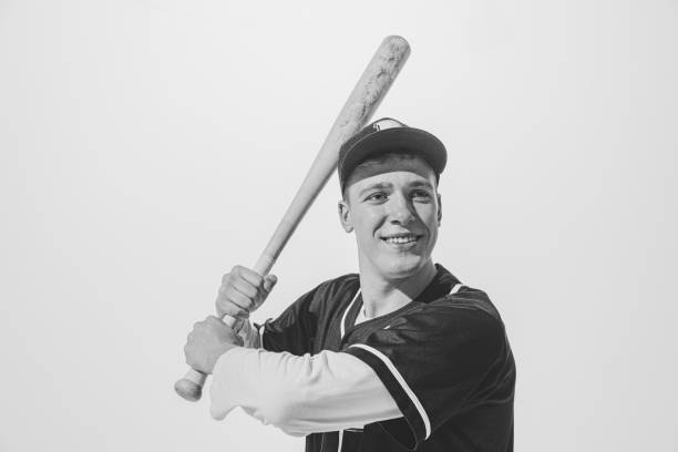 retrato en blanco y negro de un joven sonriente, jugador de béisbol en uniforme con bate preparándose para golpear la pelota. deportista motivado - men baseball baseball cap baseball bat fotografías e imágenes de stock