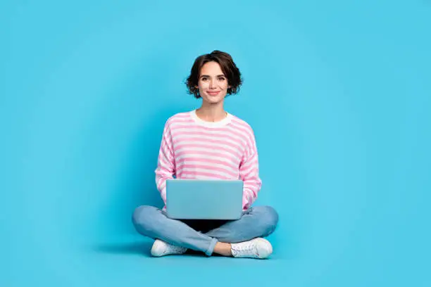 Photo of cheerful girl sitting floor browsing online working on new project document isolated on blue color background.