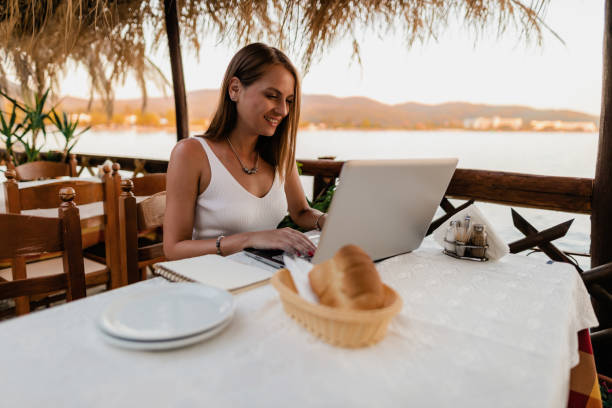 istock Young woman using a laptop in a restaurant at the seaside 1413819875