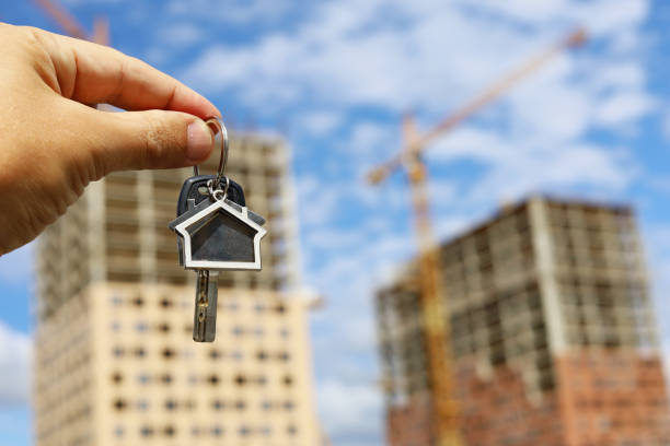 Keychain in house shape and key in male hand on background of construction cranes and new buildings stock photo