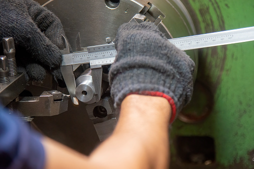 Close up scene the operator measuring metal shaft parts by  Vernier caliper. The quality control on turning machine.