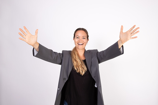 Portrait of happy young businesswoman stretching arms. Caucasian woman wearing gray suit coat and black blouse looking at camera in joy. Success and happiness concept