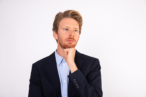 Portrait of pensive young Caucasian businessman standing with hand on chin. Manager wearing blue shirt and black suit coat standing and thinking about something. Solving problem concept