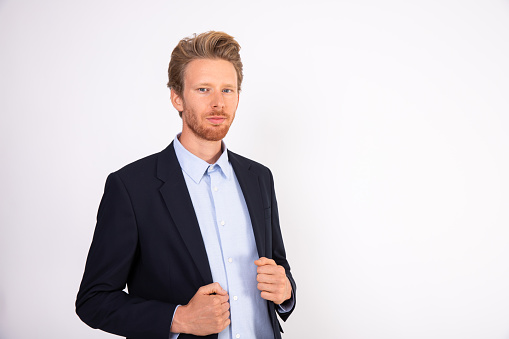 Portrait of young successful businessman looking at camera. Caucasian bearded man wearing blue shirt and black suit coat standing and smiling at camera. Successful businessman concept