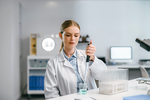 Serious, smart and intelligent scientist doing a test experiment with lab glassware equipment. Female medical research expert in science biology analyzing samples with test tube syringe in laboratory