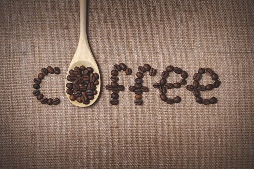 Flat lay composition of coffee beans and wooden spoon on burlap fabric. Concept from laid out word in culinary style symbolizing drinks. Top view close-up.