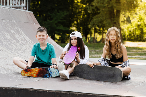 Kids smile and laugh and have fun together. Children with skateboard and penny boards communicate and discuss on the sports playground. Boy and girls friendship concept