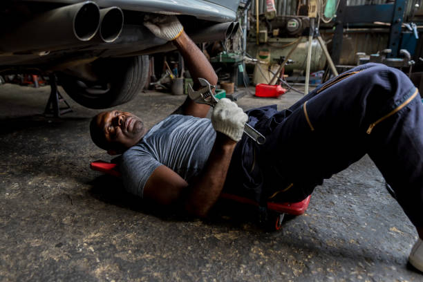 mechaniker liegt und arbeitet unter dem auto in der autowerkstatt. techniker fahrzeugwartung und überprüfung unter auto in der kfz-garage. - mechanic auto repair shop manual worker men stock-fotos und bilder