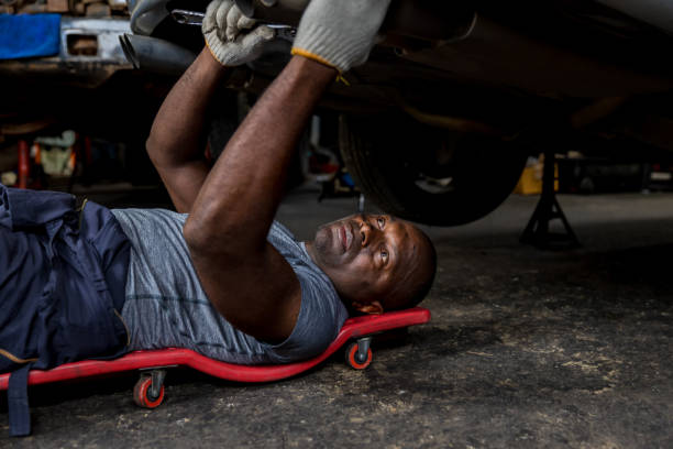 istock Mechanic lying down and working under car at auto service garage. Technician vehicle maintenance and checking under car at automotive motor garage. 1413826875