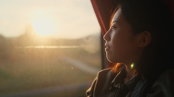 A young female tourist is sitting at a window seat in a bus and looking at the view through the window.