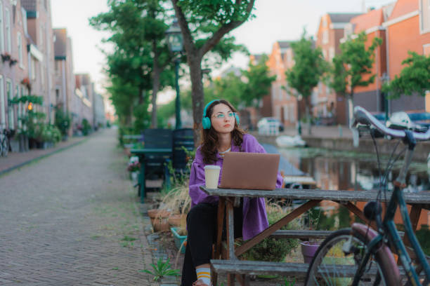 mujer sentada en la mesa al aire libre y trabajando con una computadora portátil - amsterdam canal netherlands dutch culture fotografías e imágenes de stock
