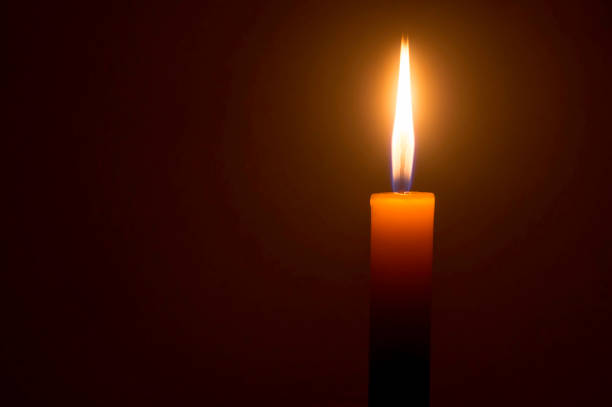 istock A single burning candle flame or light glowing on a yellow candle isolated on red or dark background on table in church for Christmas, funeral or memorial service 1413829940