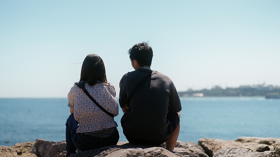 Two young tourist couple is sitting by the sea during their travel.
