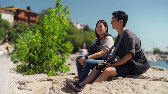 Two young tourist couple is sitting by the sea during their travel.