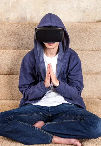 Young Man in VR Glasses sit and pray on the Sofa