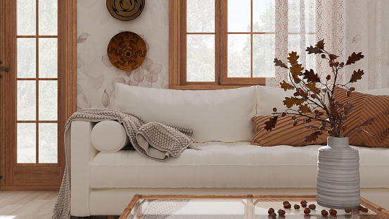 Vintage living room in white and beige tones closeup. Sofa, rattan table with autumn decors. vase with dry leaves and acorns. Boho chic design, fall interior concept