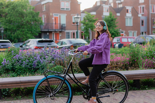 Young Caucasian woman riding bicycle in the city at sunset while listening to music in headphones